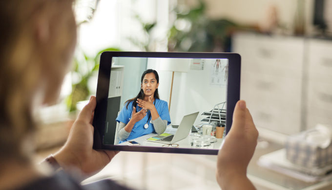 Over the shoulder shot of a patient talking to a doctor using of a digital tablet - telemedicine concept