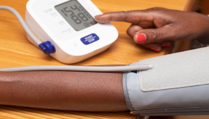 A close up view on the forearm of an African woman as she takes the readings from a blood pressure monitor, the reading falls just above the healthy range, suggesting hypertension.